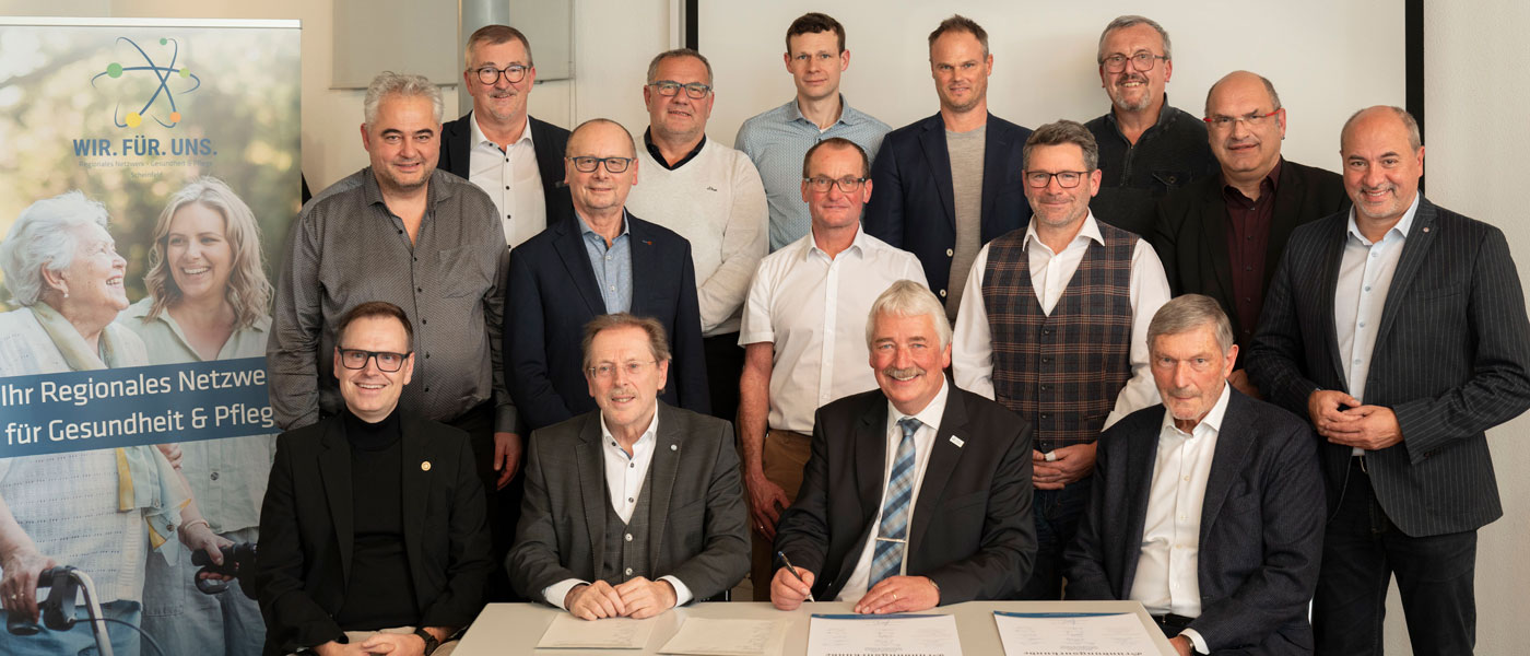 Gründungsveranstaltung der WIR.FÜR.UNS. UG. Eine Gruppe von Männern steht und sitzt um einen Tisch, auf dem Dokumente unterzeichnet werden.