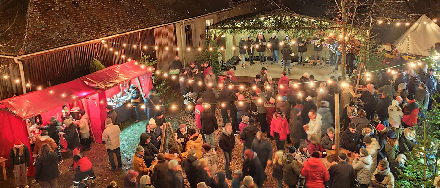 Große Menschentraube an weihnachtlich erleuchteten Buden auf einem Weihnachtsmarkt