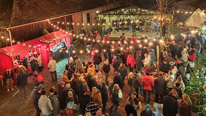 Große Menschentraube an weihnachtlich erleuchteten Buden auf einem Weihnachtsmarkt