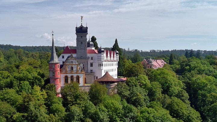 Blick aus der Vogelperspektive auf Schloss Schwarzenberg umgeben von satt grünem Wald