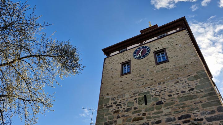 Der sanierte Torturm in Scheinfeld mit massiver Steinfassade und Turmuhr unter blauem Himmel.