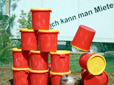 Stapel roter Plastikeimer wird durch einen Ball umgeschossen