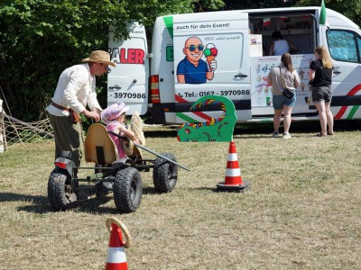 Kind wird auf einem Kinderfahrzeug über einen Parcours auf einer Wiese geschoben